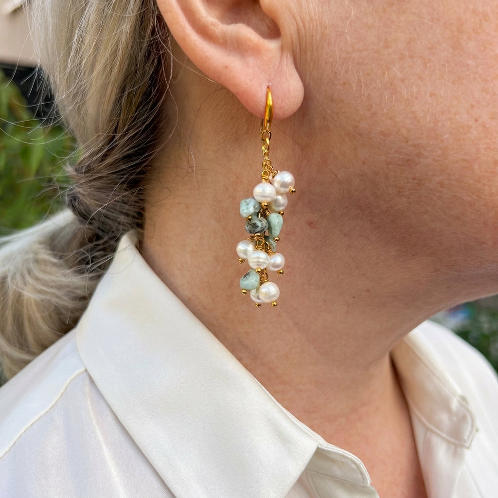 Long cluster drop earring worn on an ear, featuring white baroque pearls and pale blue-green stones suspended from gold-filled links and a curved hook.