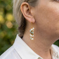 Long cluster drop earring worn in sunlight, with white baroque pearls and pale blue-green stones dangling from gold-filled links below the earlobe.