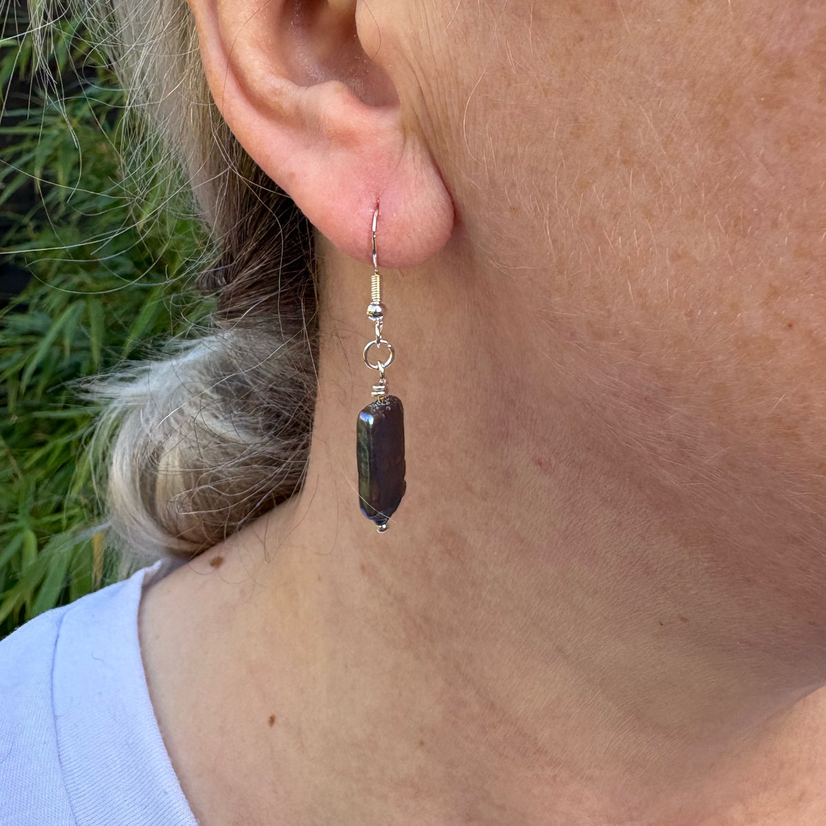 Side view of a dark blue square baroque pearl drop earring worn below the earlobe, showing its slim profile and sterling silver hook.