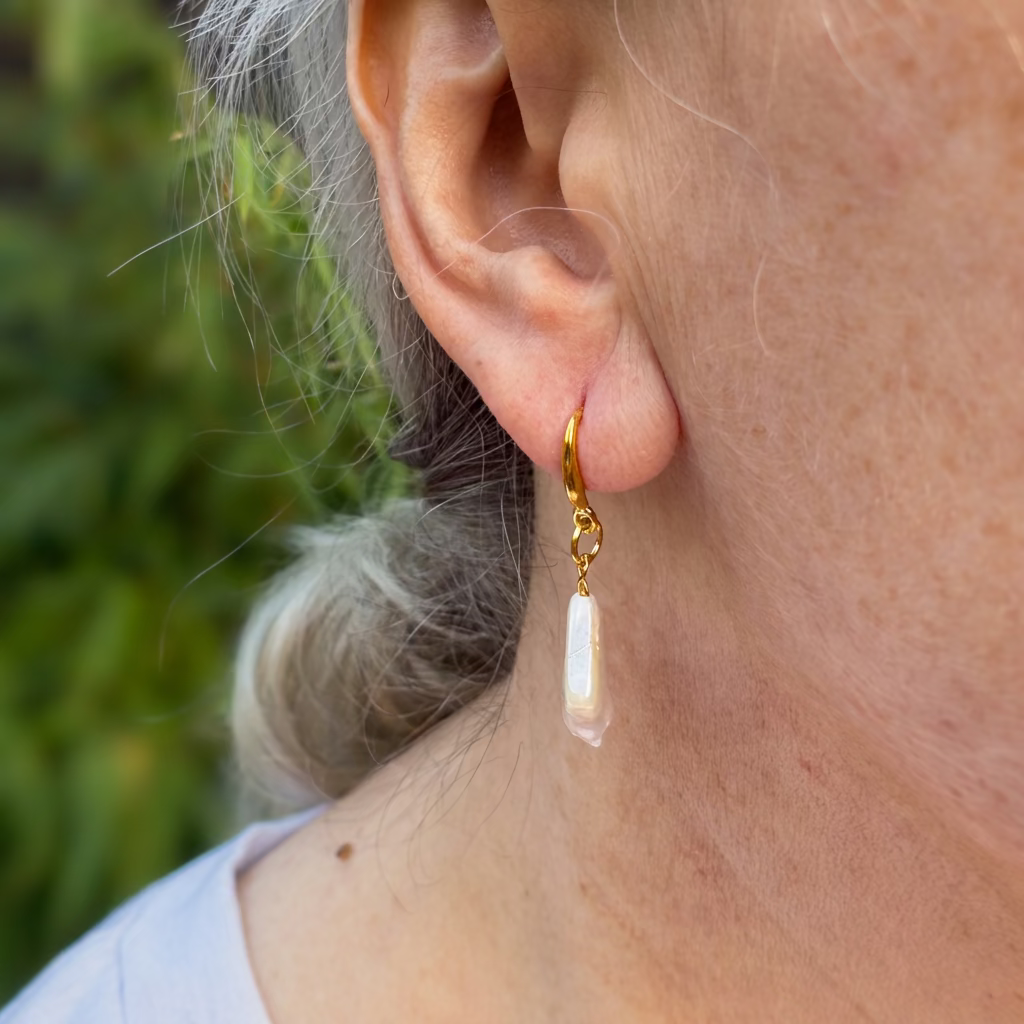 Side view of a white square baroque pearl drop earring worn on an ear, showing its slim profile, soft iridescent sheen and gold-filled hook.