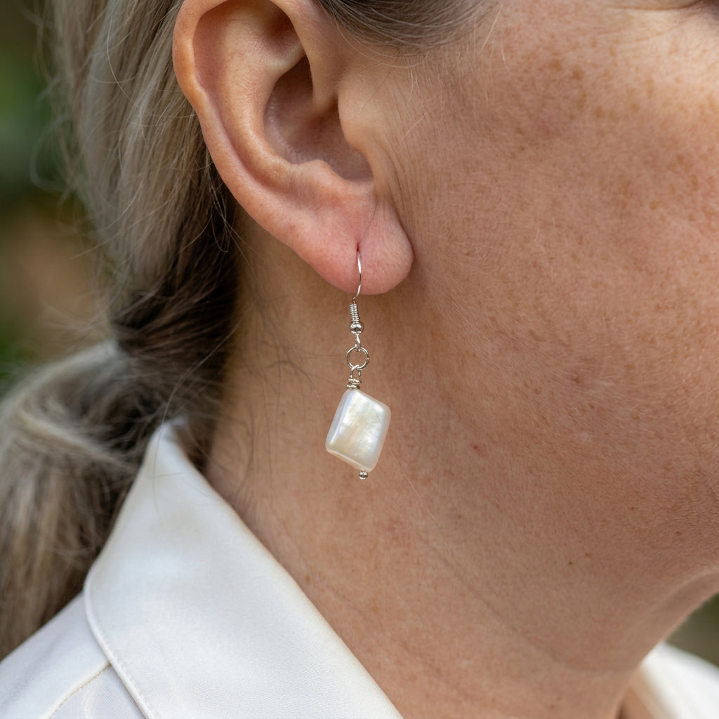 Side view of a white square baroque pearl drop earring worn on an ear, showing its slim profile, soft nacre sheen and sterling silver hook.
