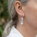 Three pale blue aquamarine beads above a creamy white baroque pearl, suspended from a crystal-set sterling silver stud, shown worn above a white shirt collar.