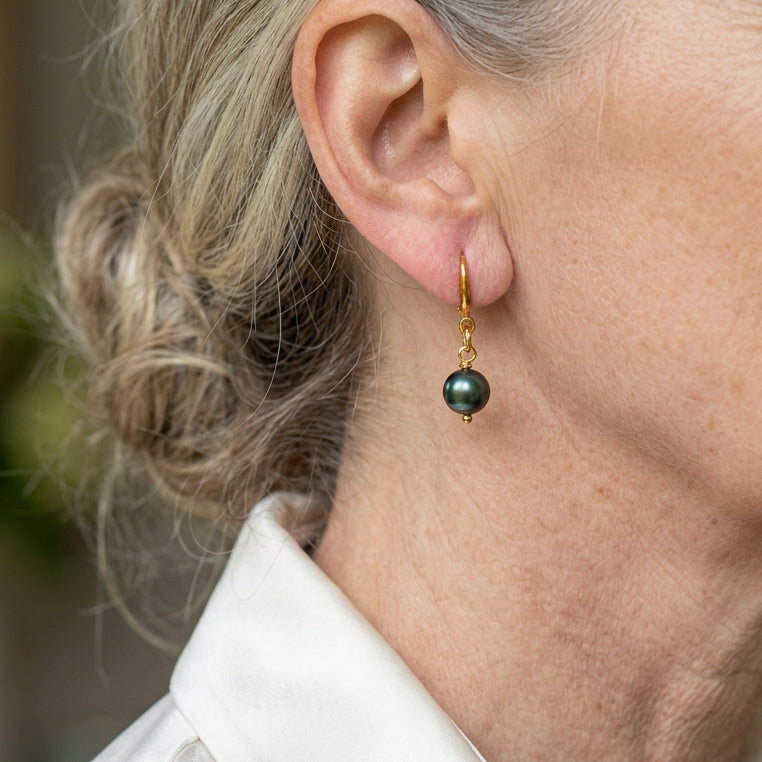 Peacock pearl drop earring on a gold-filled hook, shown worn above a white shirt collar, highlighting the pearl’s deep green colour and glossy iridescent lustre.