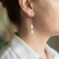 Two creamy white baroque pearls separated by a textured gold-tone spacer on a sterling silver hook, shown worn above a white shirt collar.