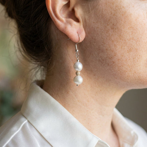 Two creamy white baroque pearls separated by a textured gold-tone spacer on a sterling silver hook, shown worn above a white shirt collar.