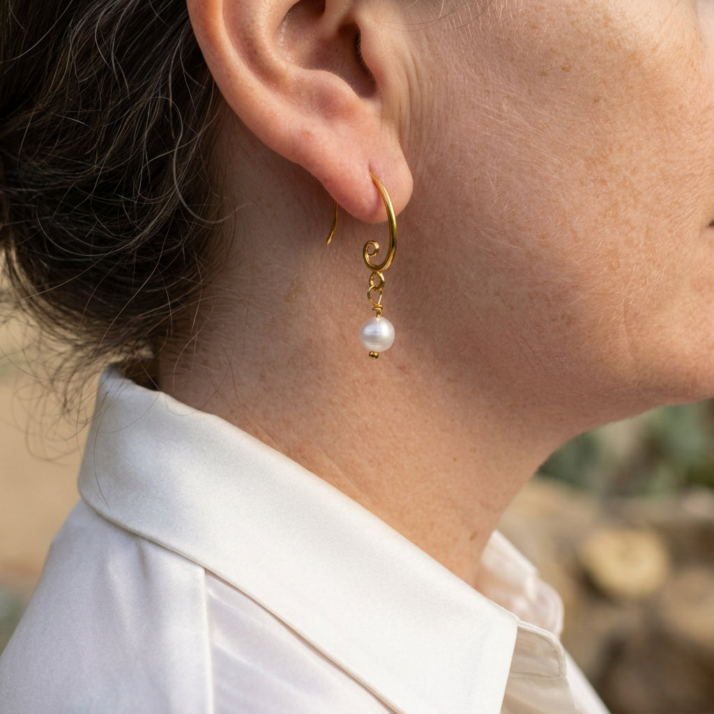 White baroque pearl drop earring worn on an ear, showing a gold-filled hook with a spiral detail, wire-wrapped link and small gold bead tip.