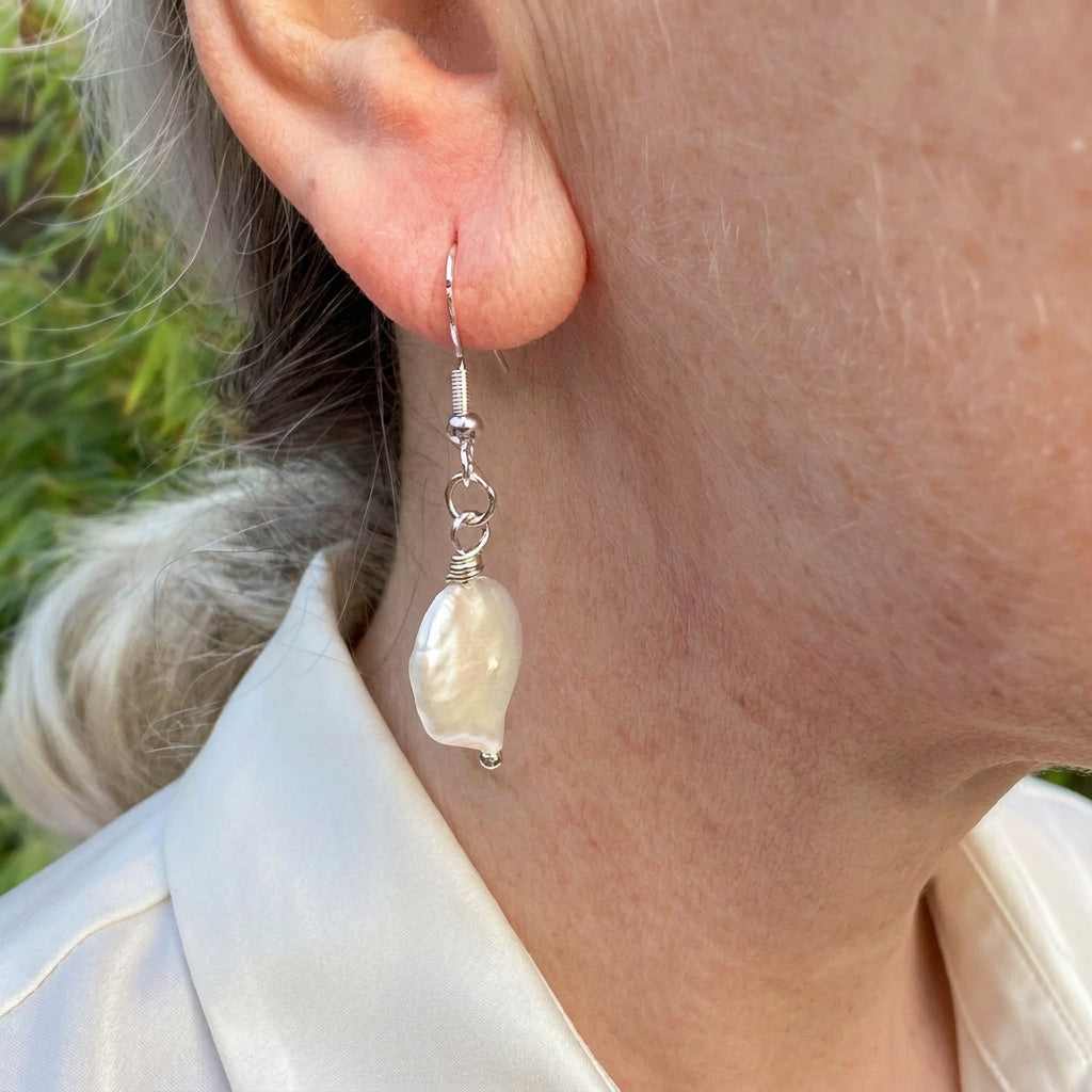 White coin pearl drop earring worn on an ear, shown at an angle with a soft nacre sheen, sterling silver hook and connecting rings.