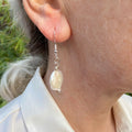 White coin pearl drop earring worn on an ear, shown at an angle with a soft nacre sheen, sterling silver hook and connecting rings.