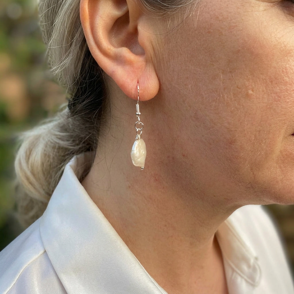 Side view of a white coin pearl drop earring worn on an ear, showing its slim profile, soft nacre sheen and sterling silver hook with connecting rings.