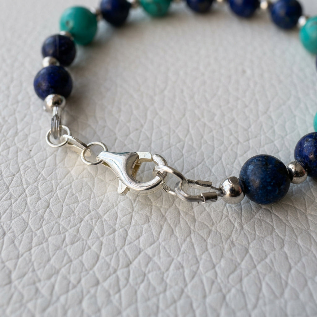 Close-up of the bracelet’s sterling silver clasp beside dark blue lapis lazuli beads on a white textured surface.