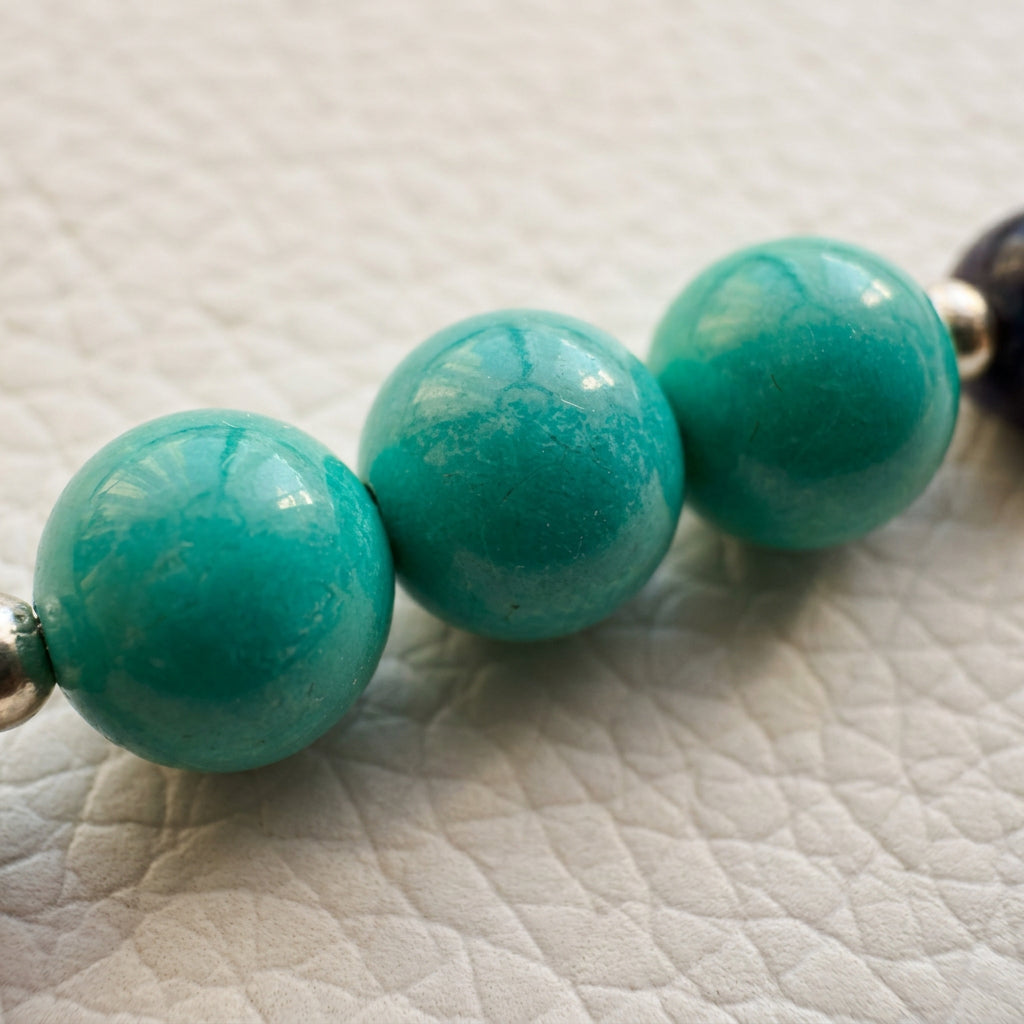Close-up of the bracelet’s green-blue Hubei turquoise and dark blue lapis lazuli beads with silver spacers on a white textured surface.