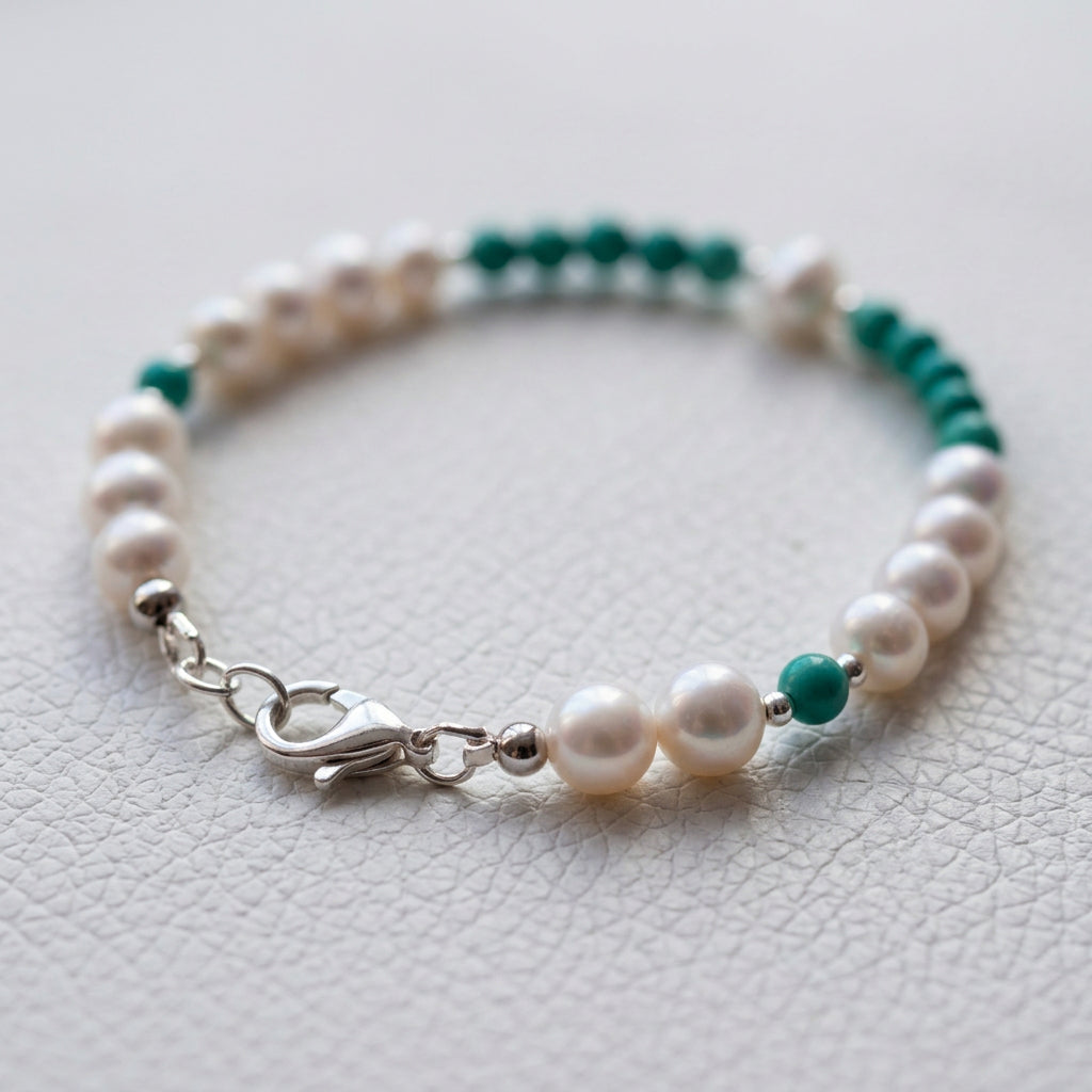 White baroque pearl and Hubei turquoise bracelet arranged in an oval, with the sterling silver clasp in the foreground on a white textured surface.