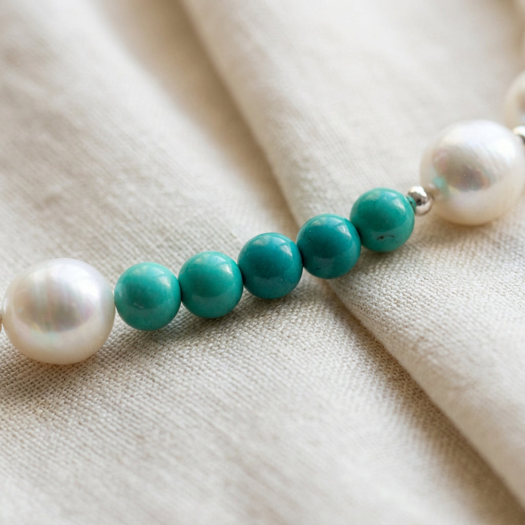 Close-up of five small Hubei turquoise beads between white baroque pearls on softly folded cream linen.