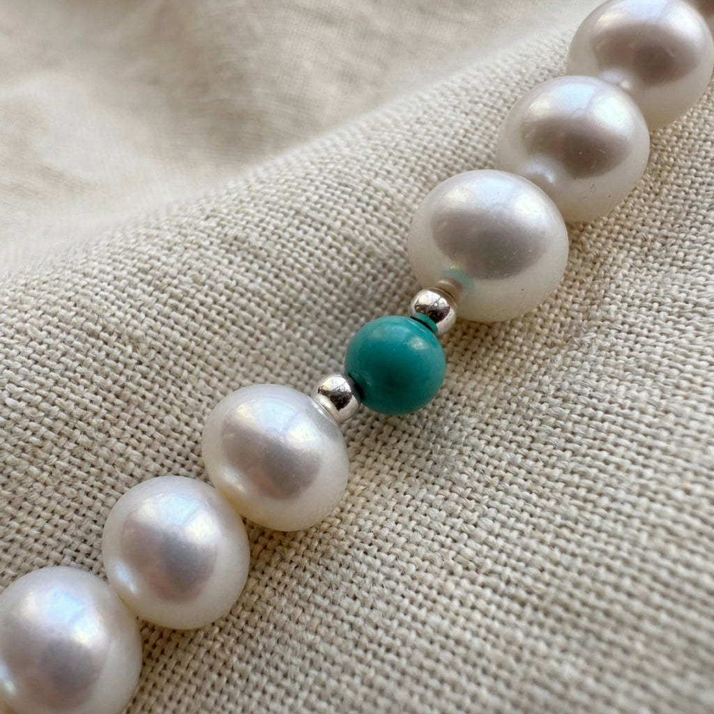 Close-up of white baroque pearls and a single Hubei turquoise bead framed by sterling silver beads on cream linen.