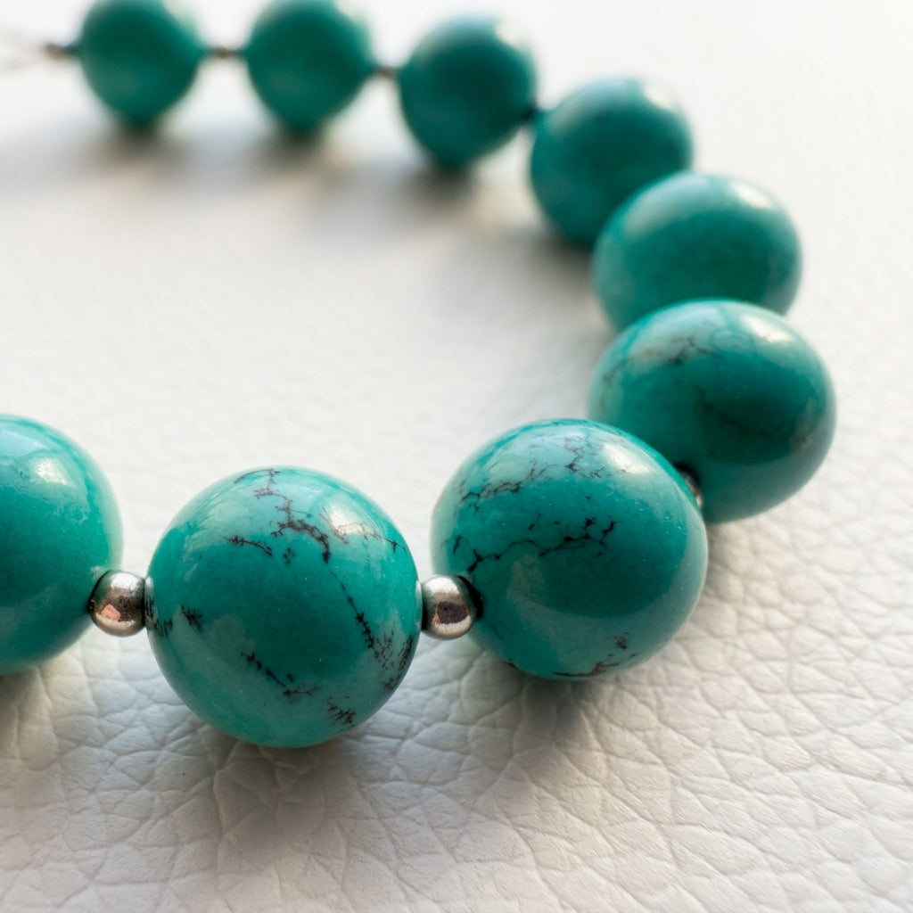 Low-angle close-up of Hubei turquoise and sterling silver beads on a white textured surface.