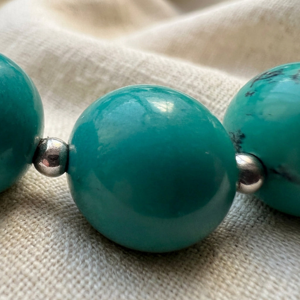 Macro view of a polished Hubei turquoise bead between two small sterling silver beads on cream linen.