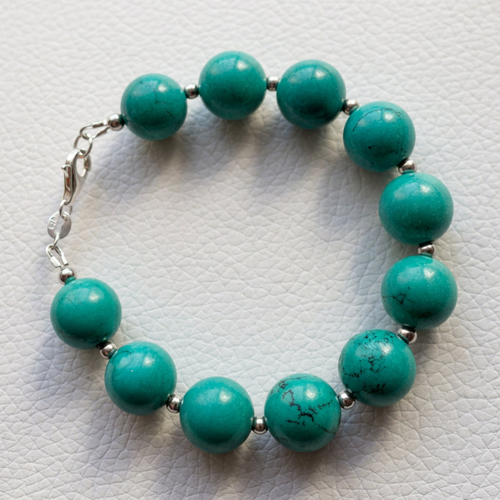 Full view of the Hubei turquoise bracelet arranged in a circle, showing sterling silver beads and clasp on a white textured surface.