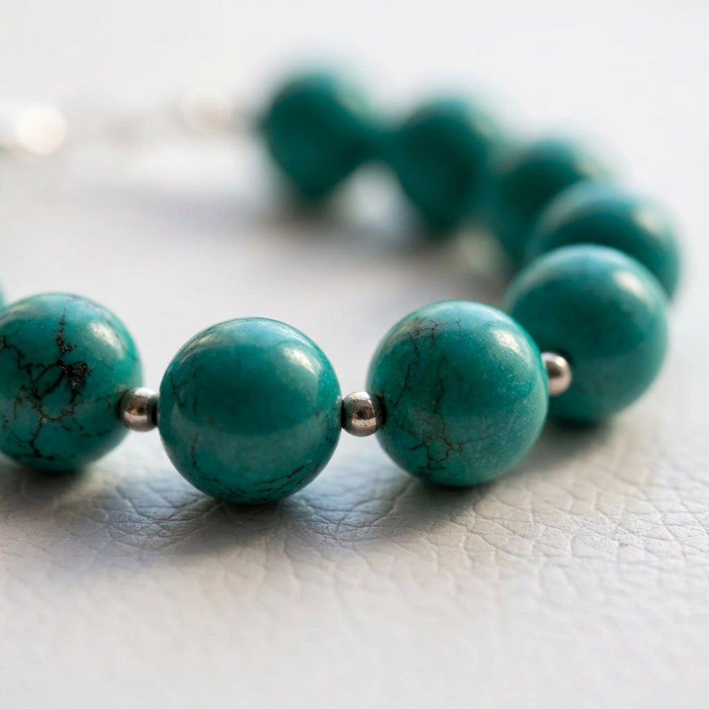 Close-up of dark branching markings on Hubei turquoise beads with sterling silver beads on a white textured surface.