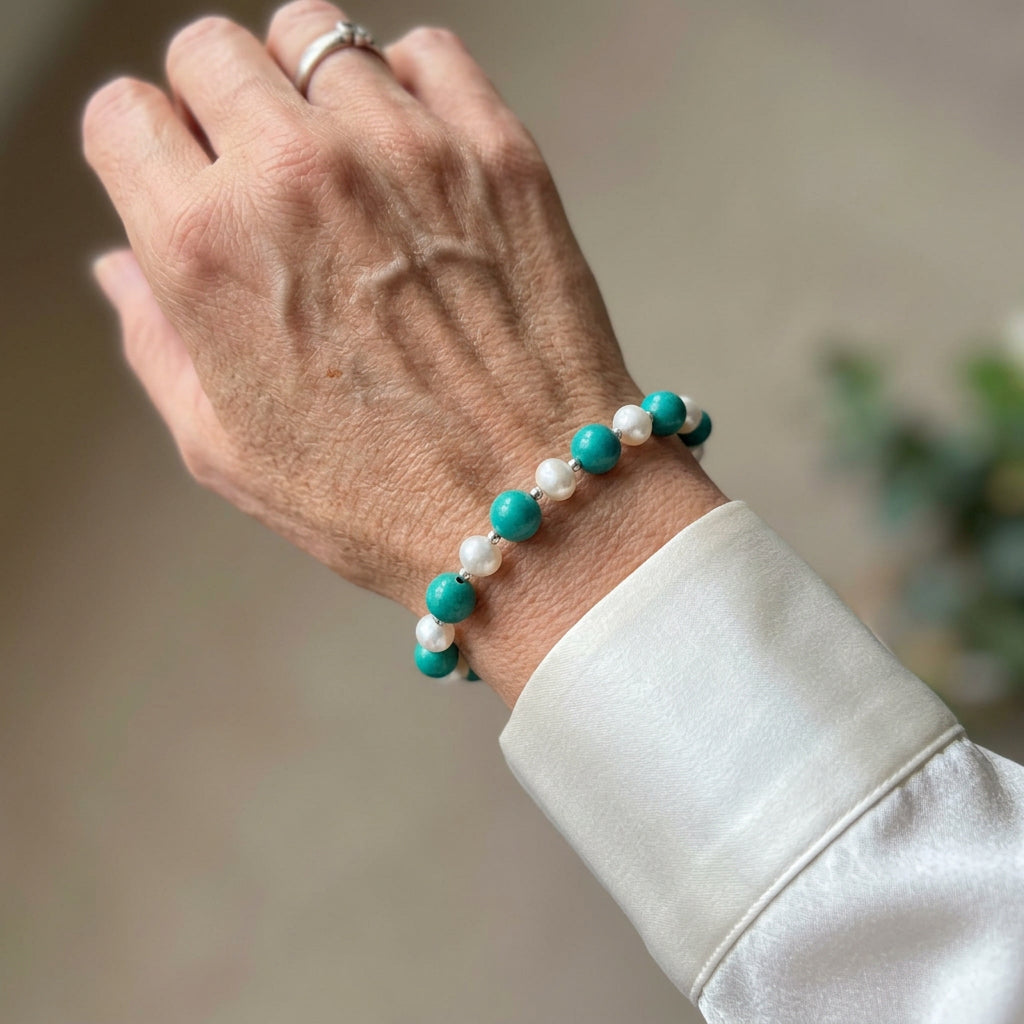 Hubei turquoise and white baroque pearl bracelet with sterling silver beads worn on a raised wrist beside a white cuff.