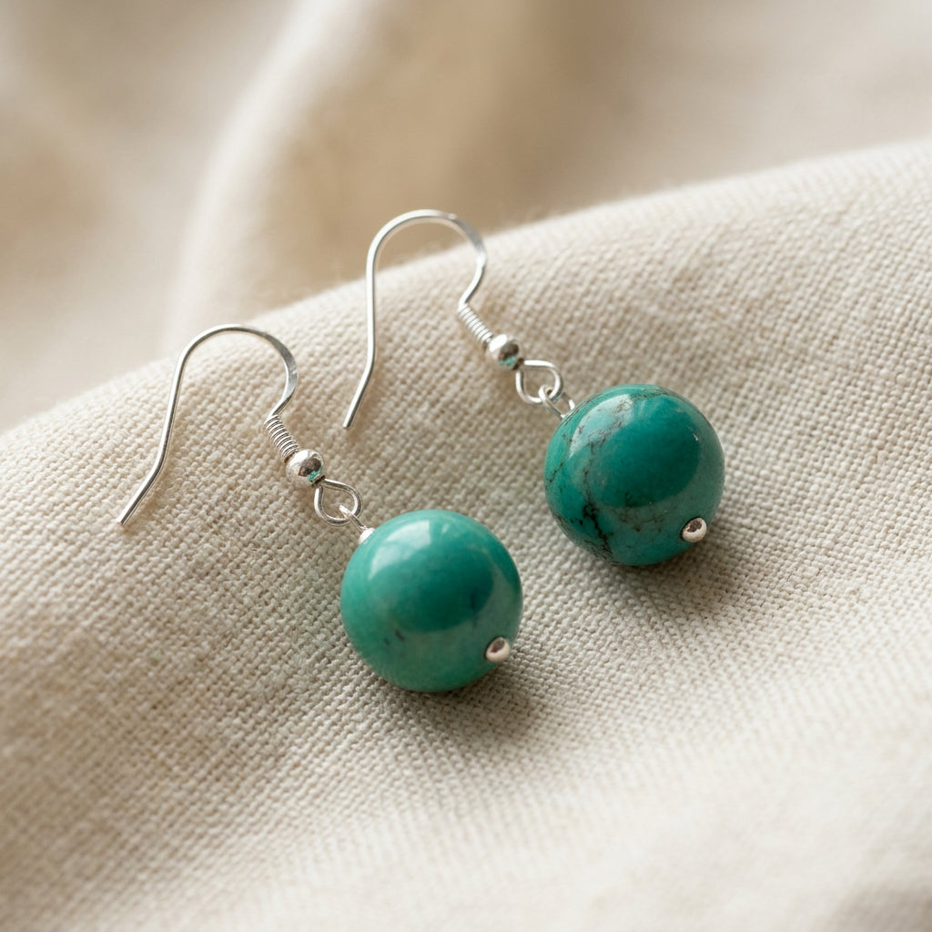 Pair of stabilised Hubei turquoise drop earrings with round green-blue beads and sterling silver hooks on softly folded cream linen.