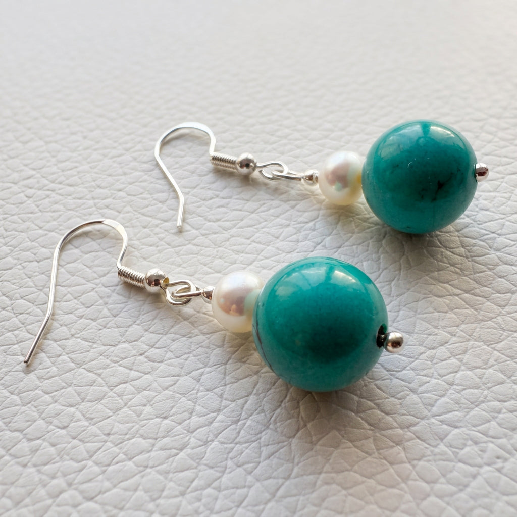 Pair of white baroque pearl and Hubei turquoise drop earrings with sterling silver hooks, laid flat on a white textured surface.