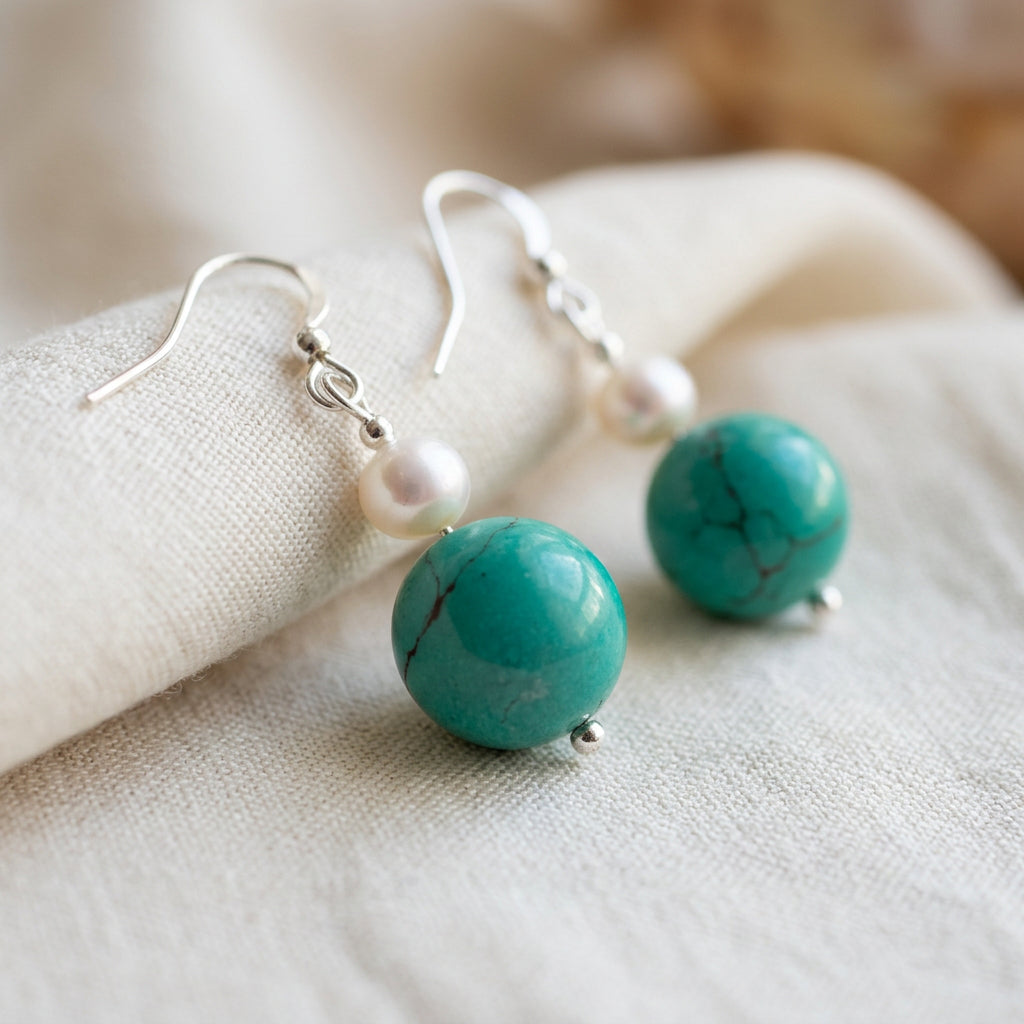 Close-up of white baroque pearl and Hubei turquoise earrings with sterling silver hooks on softly folded cream linen.