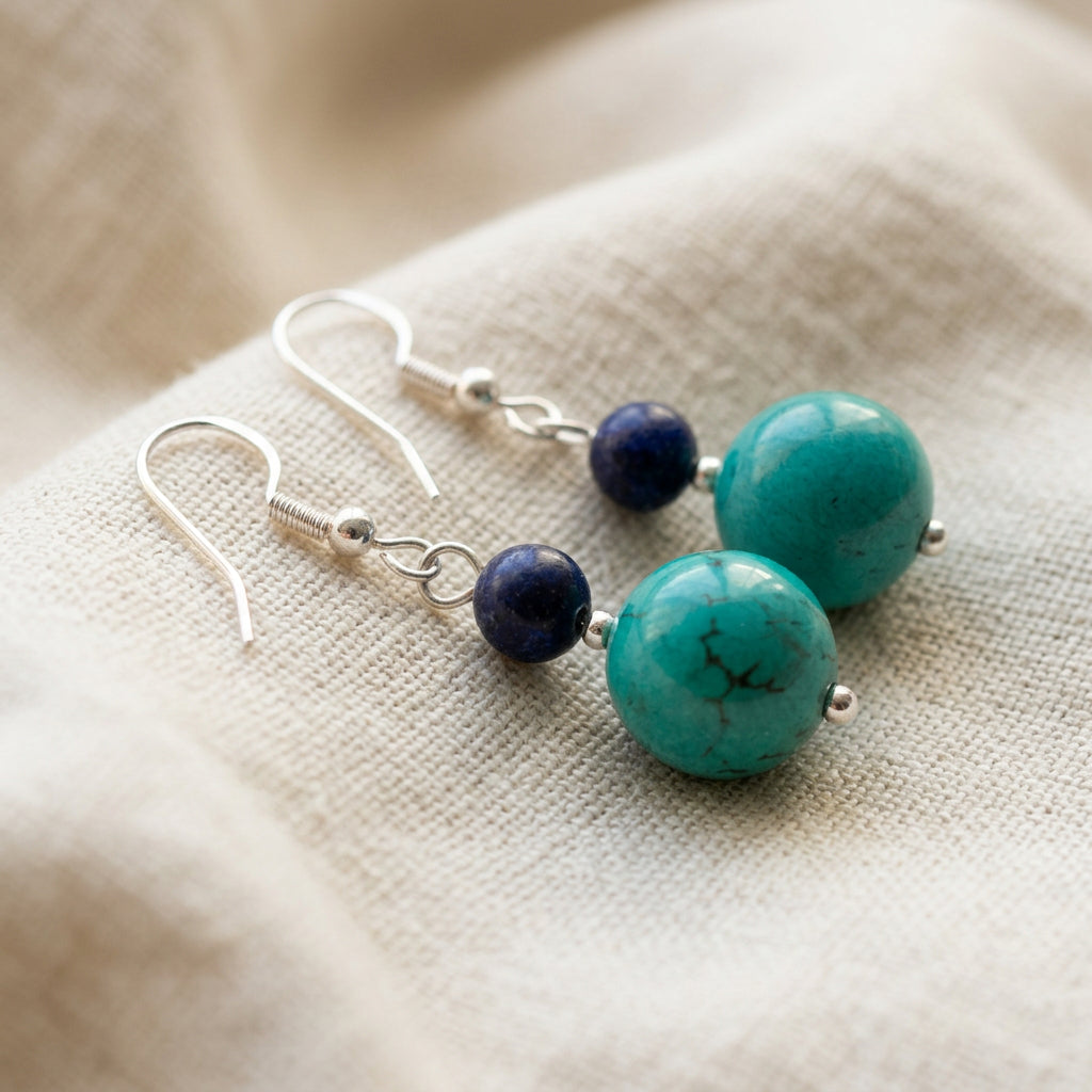 Pair of lapis lazuli and stabilised Hubei turquoise earrings with sterling silver hook fittings on a cream linen textured surface.