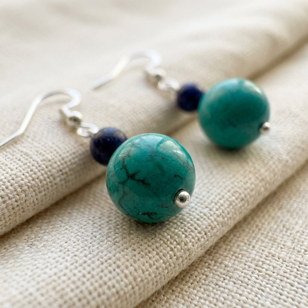 Close-up of stabilised Hubei turquoise beads with dark markings, paired with lapis lazuli and sterling silver fittings on cream linen texture.