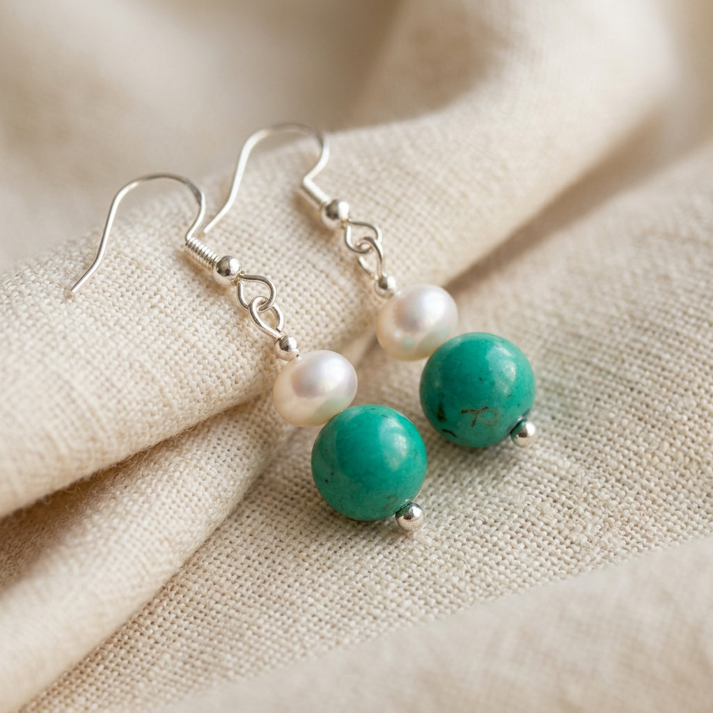 White baroque pearl and turquoise drop earrings with sterling silver hooks resting side by side on softly folded cream linen.