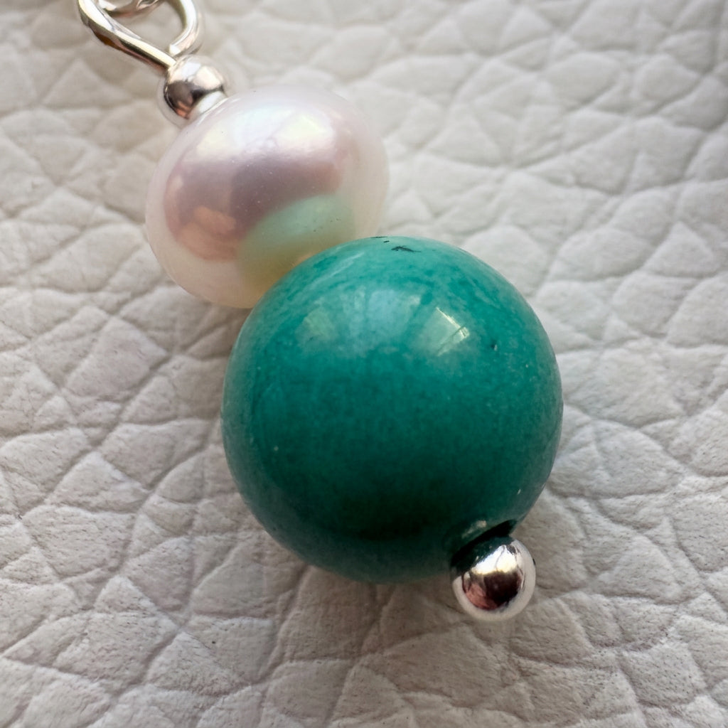Macro view of a green-blue turquoise bead beneath a white baroque pearl, with sterling silver details on a white textured surface.