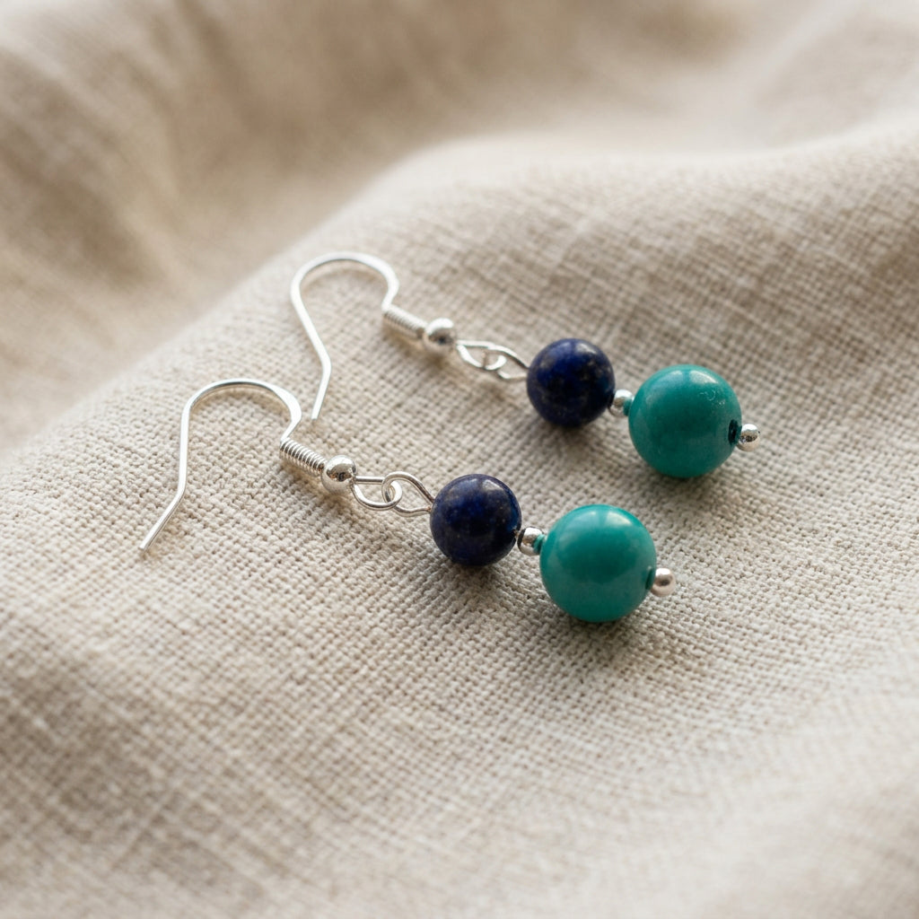 Pair of sterling silver earrings on cream linen, each with a dark blue lapis lazuli bead above green-blue Hubei turquoise.
