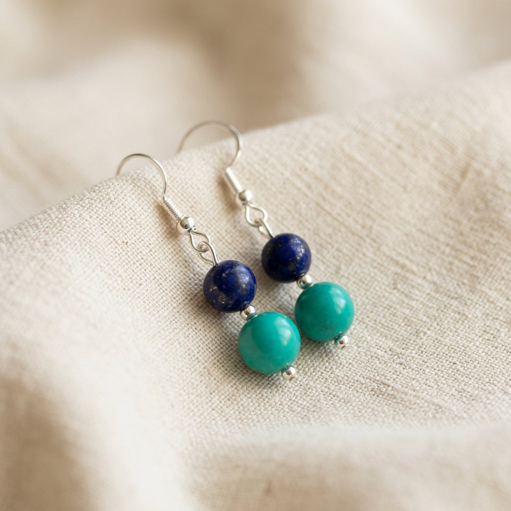 Angled view of lapis lazuli and Hubei turquoise earrings showing sterling silver hooks and spacer beads on cream linen