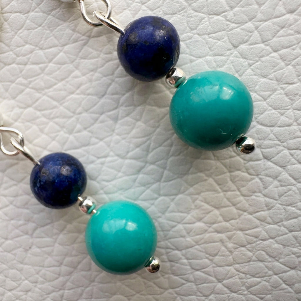 Close-up of dark blue lapis lazuli and green-blue Hubei turquoise beads separated by sterling silver beads on a white textured surface.