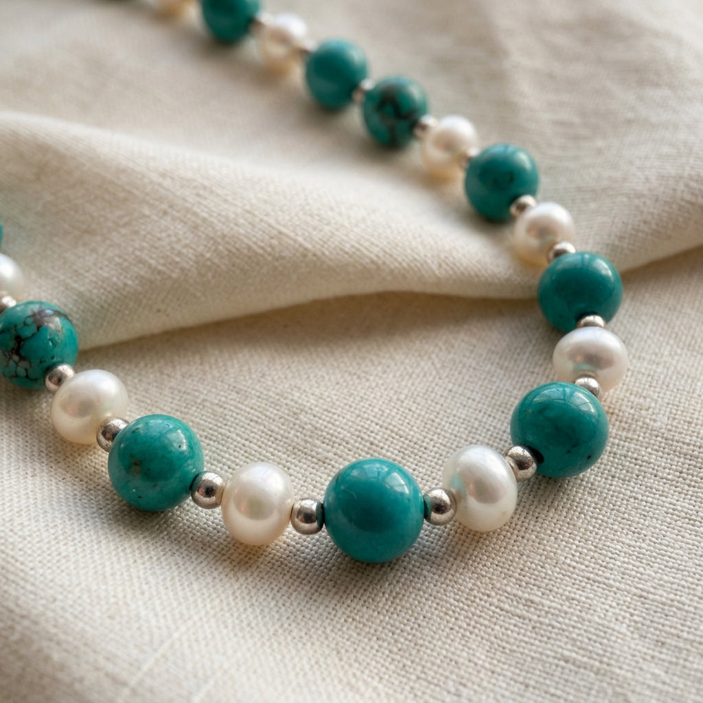 Close-up of alternating Hubei turquoise beads and white baroque pearls with silver-coloured spacers on folded cream linen.