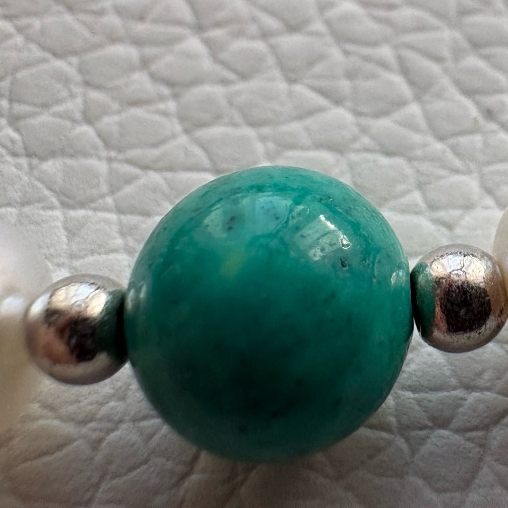 Macro view of a green-blue Hubei turquoise bead between small silver-coloured spacer beads on a white textured surface.