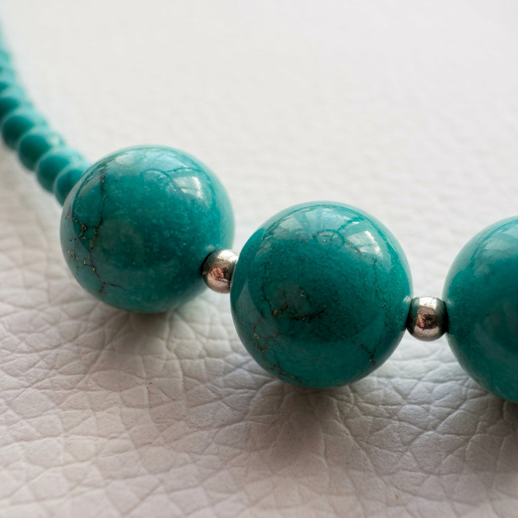 Macro view of the necklace’s large Hubei turquoise beads and silver-coloured spacers on a white textured surface.