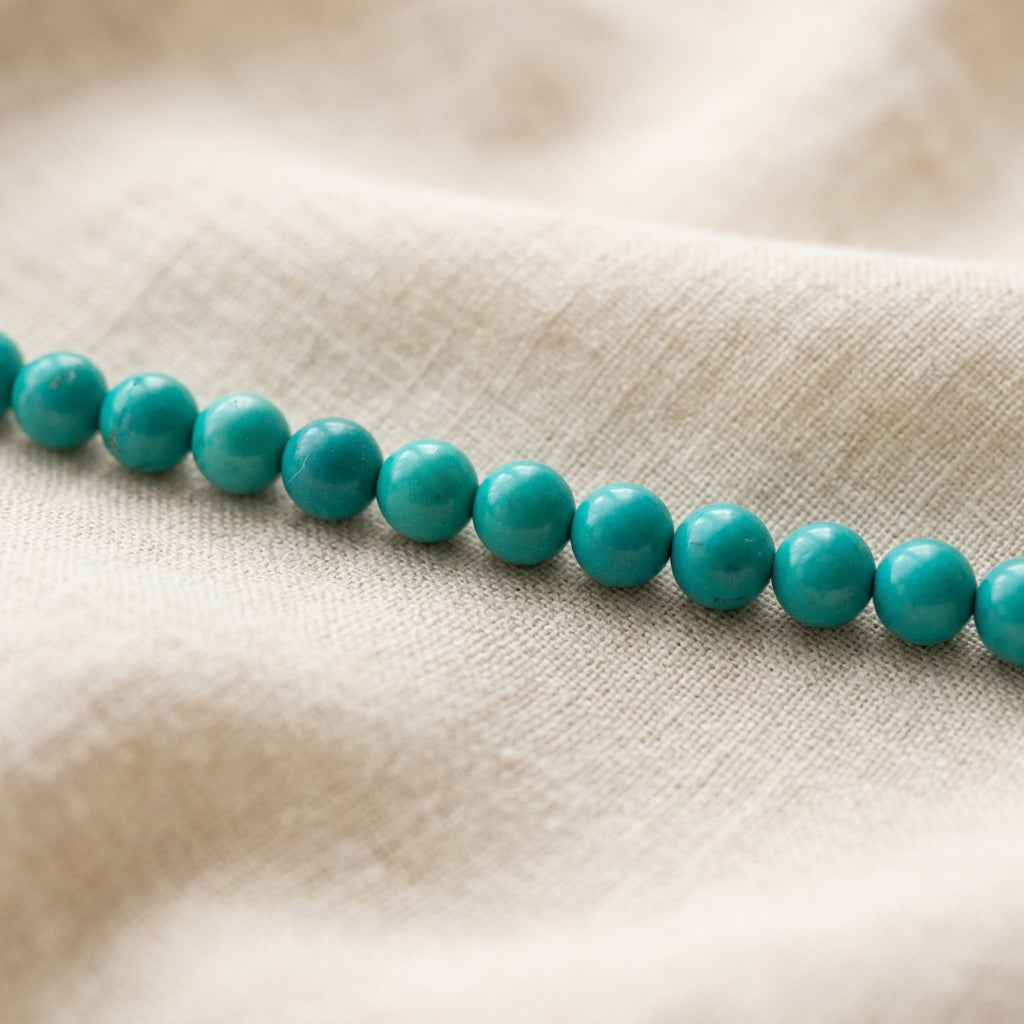 Close-up of the necklace’s small turquoise beads showing colour variations and markings on cream linen.