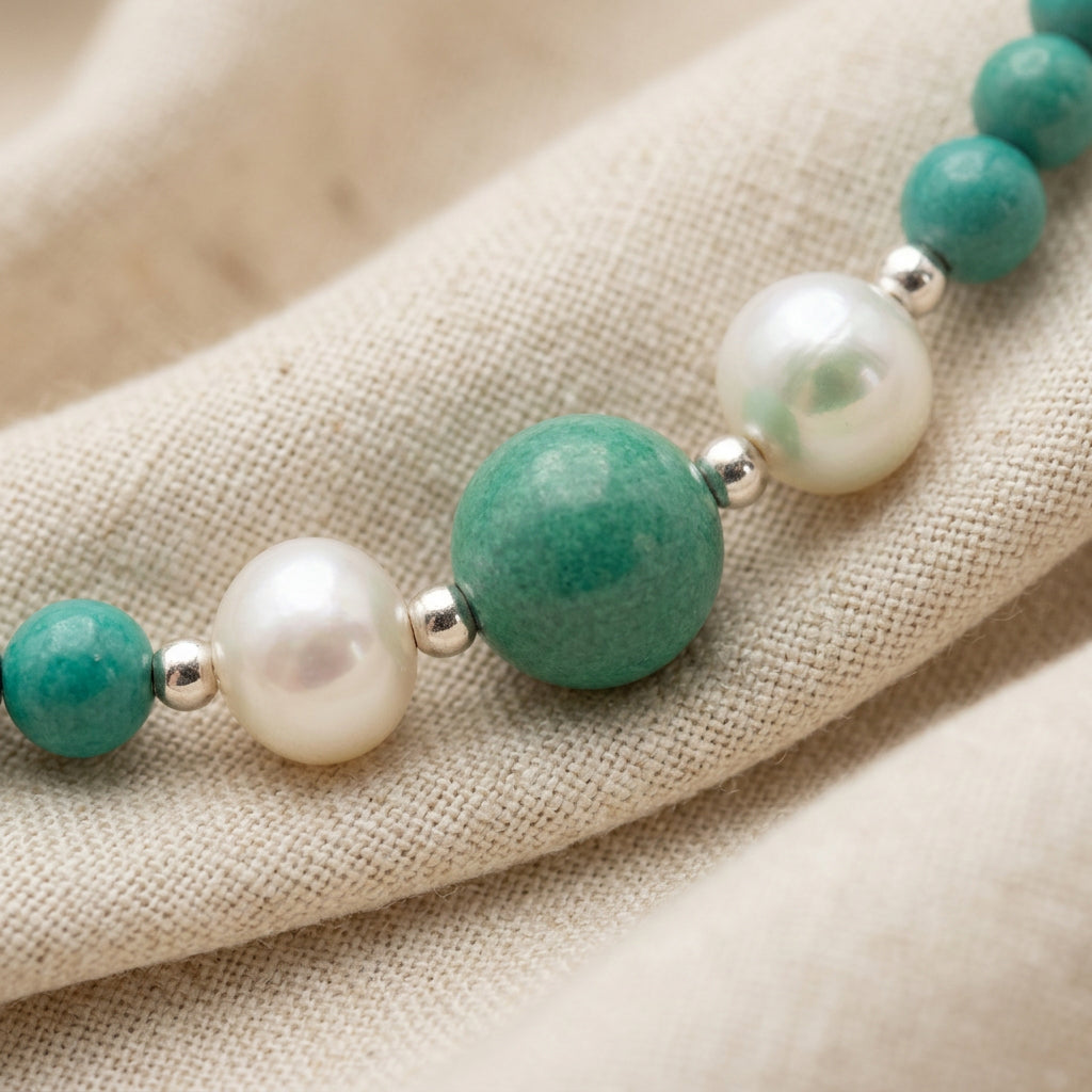 Macro view of a larger Hubei turquoise bead, two white baroque pearls and silver-coloured spacers running diagonally across cream linen.