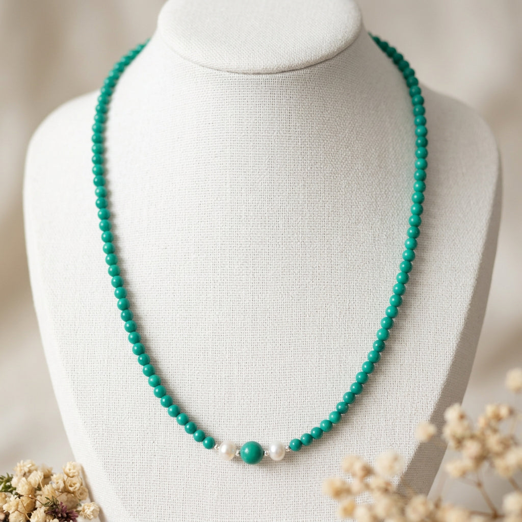 Full Hubei turquoise necklace on a white display bust beside dried flowers, with a larger central bead between two white baroque pearls.