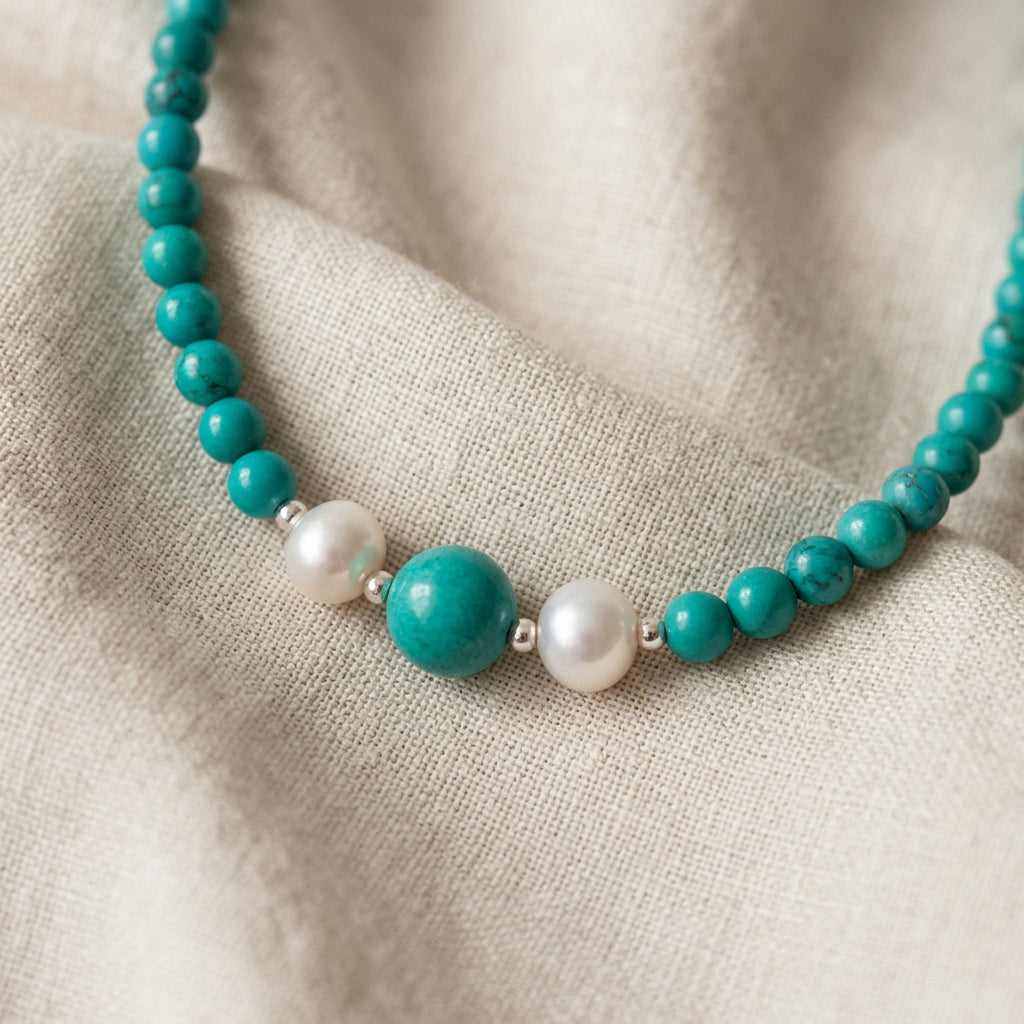 Close-up of the necklace’s larger Hubei turquoise bead between two white baroque pearls, with smaller turquoise beads on folded cream linen.