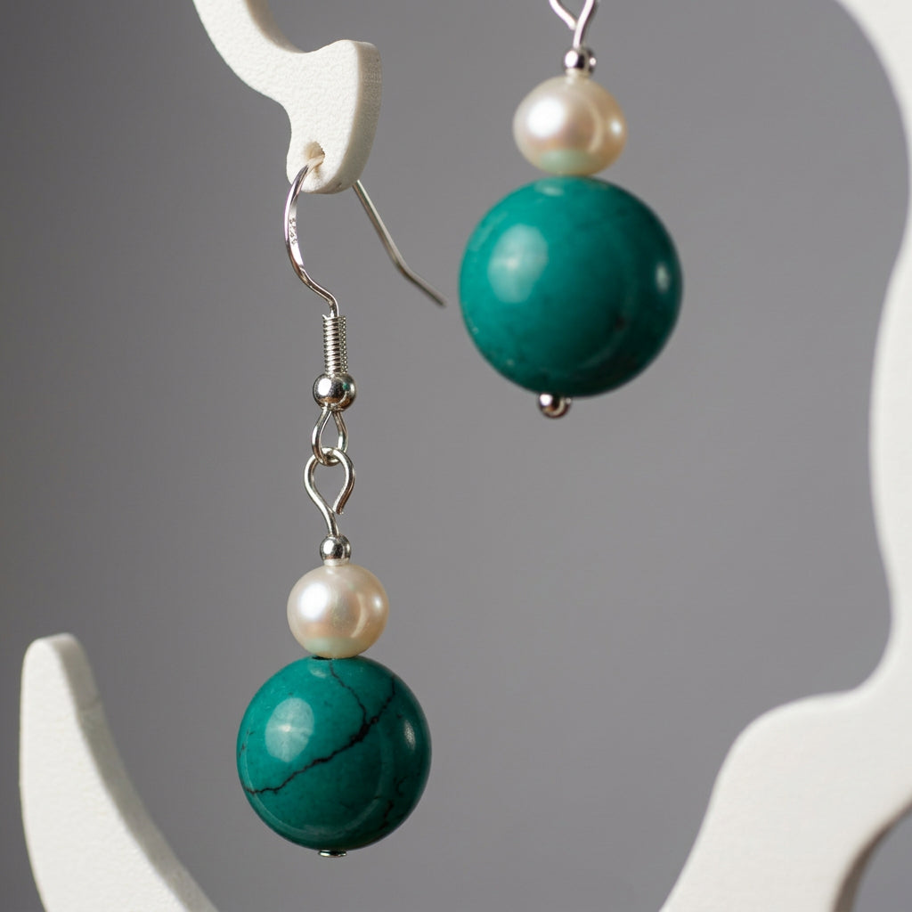 Close-up of Hubei turquoise beads with dark markings beneath white baroque pearls, hanging from sterling silver fittings.