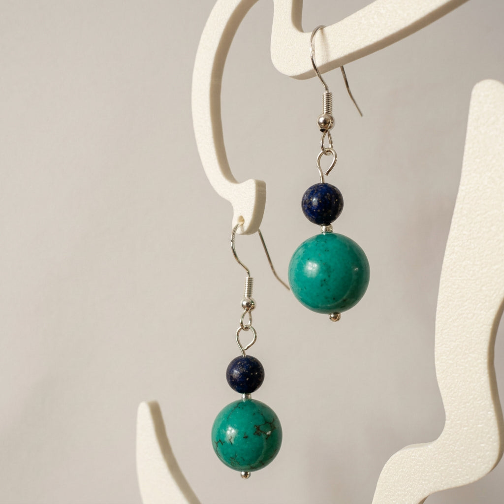 Pair of lapis lazuli and stabilised Hubei turquoise earrings with sterling silver hook fittings on a white textured surface.