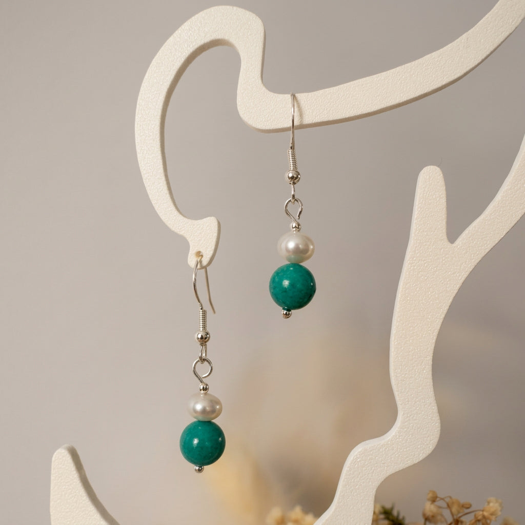 White baroque pearl and turquoise drop earrings with sterling silver hooks hanging from a cream display stand.