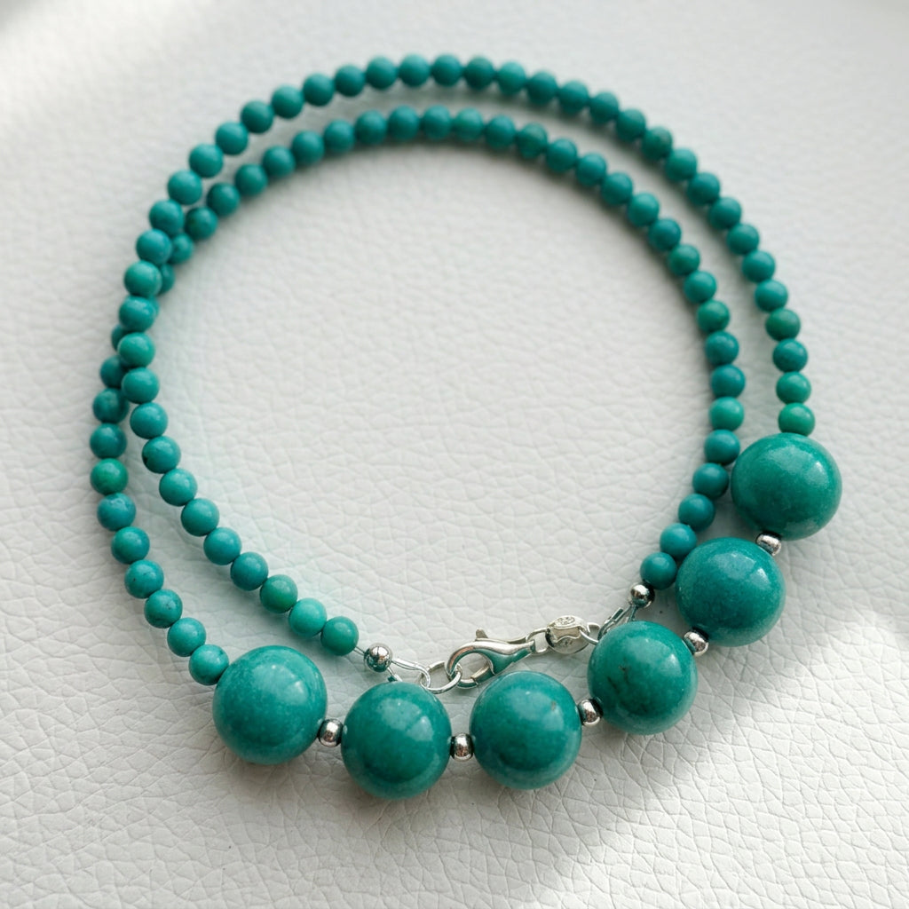 Hubei turquoise necklace arranged in overlapping loops on a white textured surface, showing six larger beads, smaller turquoise beads and a sterling silver clasp.