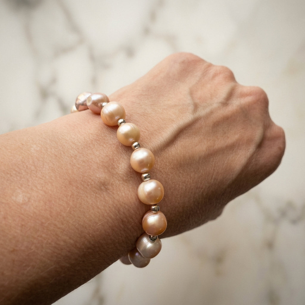 Pink baroque pearl bracelet worn on a wrist, showing lustrous pearls in peach, blush and mauve tones separated by small silver-coloured beads.