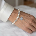 White baroque pearl and pale blue aquamarine bracelet with a clear and blue crystal snowflake charm, worn on the wrist beside a white silk shirt cuff.⠋