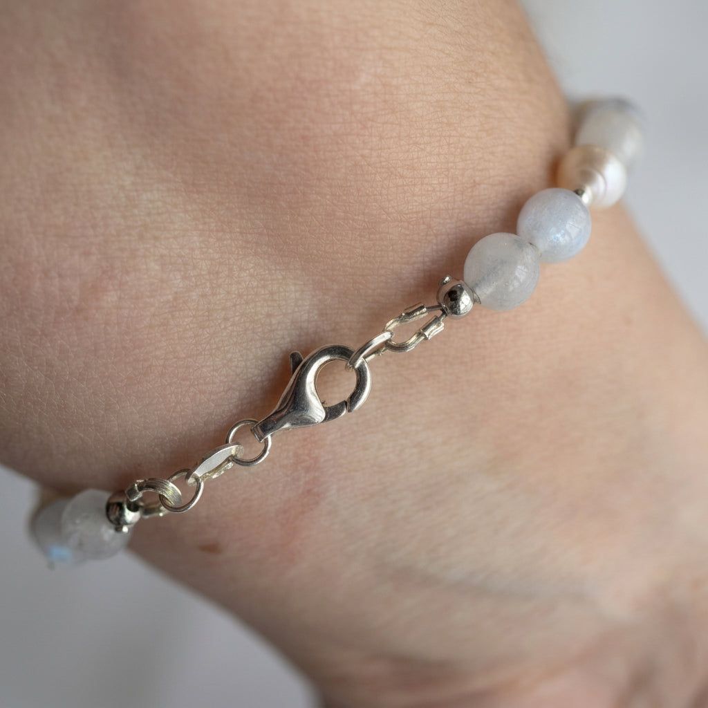Close-up of the sterling silver lobster clasp on an aquamarine and white baroque pearl bracelet worn on a wrist.