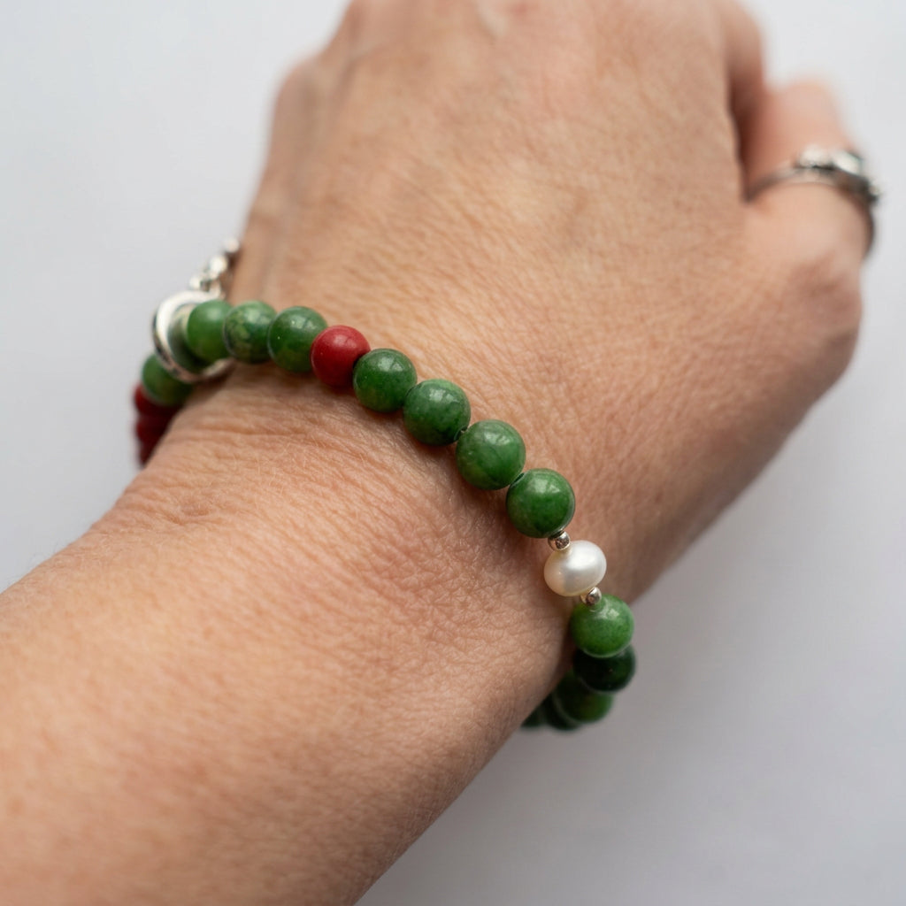 Green jade bracelet worn on a wrist, showing a single white pearl with silver-coloured spacers and red coral accents.