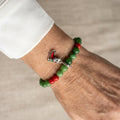 Green jade bracelet with red coral accents and a red-and-green enamel Santa’s sleigh charm, worn on the wrist beside a white silk shirt cuff.
