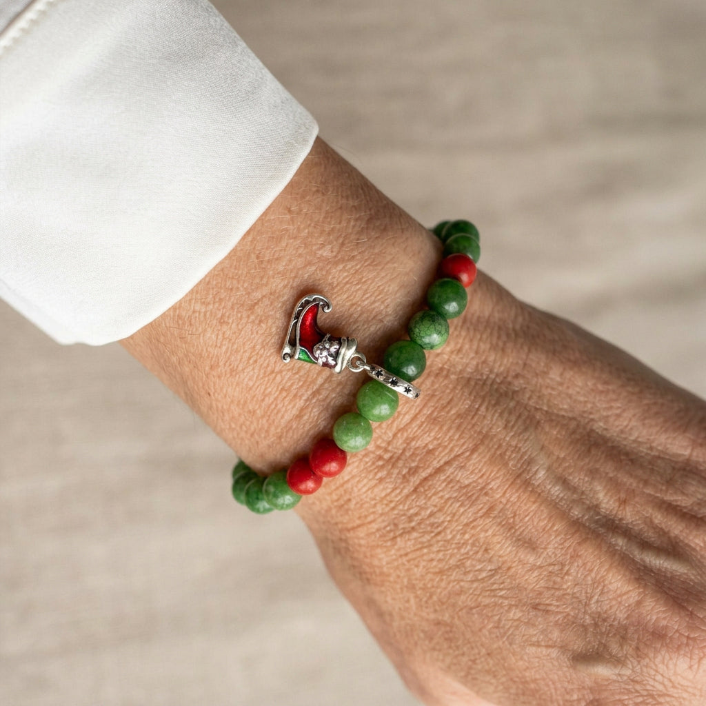 Green jade bracelet with red coral accents and a red-and-green enamel Santa’s sleigh charm, worn on the wrist beside a white silk shirt cuff.